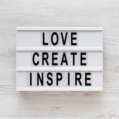 'Love create inspire' words on a modern board on a white wooden background, top view. Overhead, from above, flat lay.
