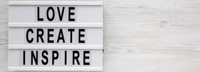 'Love create inspire' words on a lightbox on a white wooden background, top view. Overhead, from above, flat lay. Copy space.