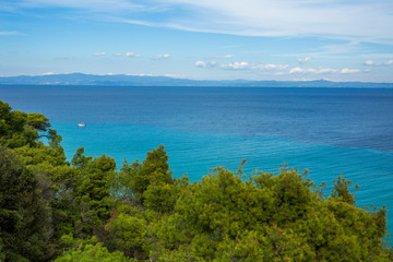 Great peaceful marine landscape of beautiful sunny scenic nature of Greece. Small white yacht seen in distance. Green forest in foreground. Horizontal color photography.