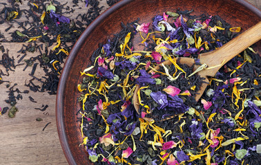blended tea. black tea with dry flower petals and fruits. dry black tea leaves in a wooden spoon on...