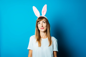 Young woman in bunny ears with a pensive face on a blue background. Easter concept