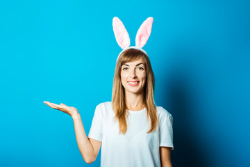 A young woman in the ears of a bunny smiles on a blue background. Easter concept