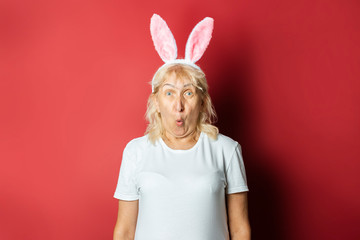 Old lady with rabbit or hare ears on a dark pink background. Easter concept. Grandmother