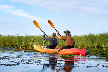 Couple (man and a woman) kayaking on a wild river among reeds and lilies