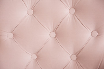 Surface of the sofa in close-up. The carriage-type tie is buttoned. Pink Chesterfield style quilted upholstery background closeup