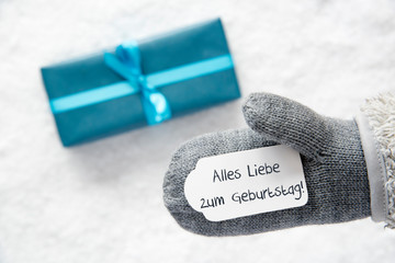 Glove With Label With German Text Alles Liebe Zum Geburtstag Means Happy Birthday. Turquoise Gift Or Present On Snow In Background. Seasonal Greeting Card.
