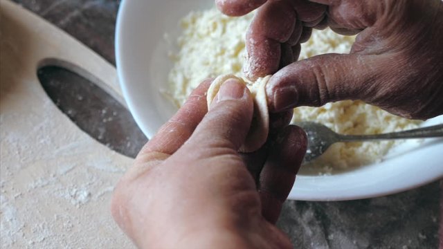 Mature female hands making dumplings with cheese at home kitchen, view from above.