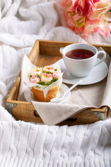 Flower cupcakes and cup of tea on wooden tray on white plaid.  Beautiful sponge cup cakes decorated with buttercream roses on white background.