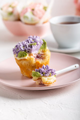 Flower cupcakes and cup of tea on white background. Beautiful sponge cup cakes decorated with buttercream lilac flower.