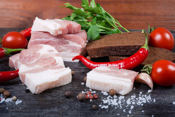 Partly sliced pork belly among spices, vegetables, brown bread, closeup