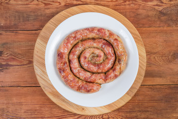 Baked spiral pork sausage on dish on wooden serving board