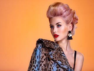 Beautiful woman with style hairstyle. White woman with bright colored makeup. Fashionable young woman is in the spotted fur coat. Stunning blonde girl. Bright eye makeup. Attractive sexy model poses