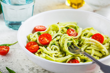 Zucchini pasta with pesto, avocado and tomatoes in white plate. Raw vegan food concept.