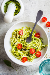Zucchini pasta with pesto, avocado and tomatoes in white plate, top view. Raw vegan food concept.