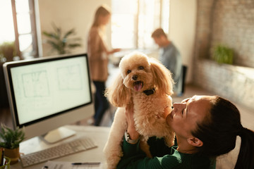 Happy Asian freelance worker having fun with her poodle in the office.