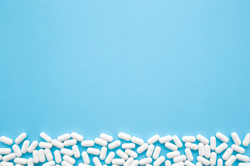 White pills on light pastel blue table. Medical, pharmacy and healthcare concept. Closeup. Empty place for text or logo. Top down view.