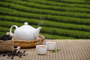 Warm cup of tea with teapot, green tea leaves and dried herbs on the bamboo mat at morning in...