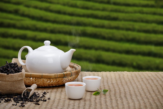 Warm cup of tea with teapot, green tea leaves and dried herbs on the bamboo mat at morning in plantations background with empty space, Organic product from the nature for healthy with traditional