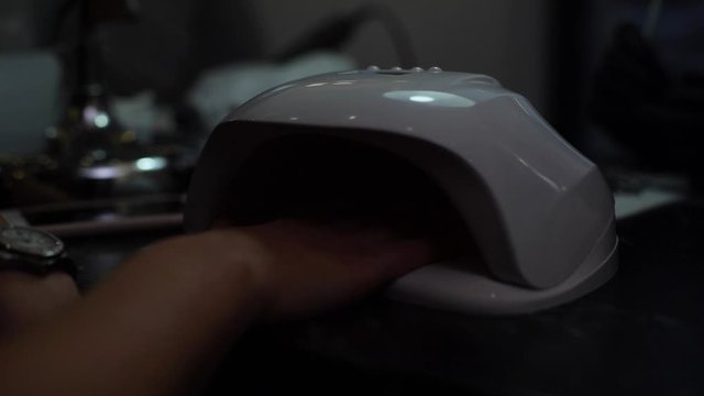Woman dries her nails with shellac in UV lamp in nail care salon, close-up. Shooting in slow motion.