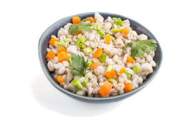 Pearl barley porridge with vegetables in blue ceramic bowl isolated on white background. Side view, close up.