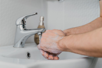 wash your hands with soap under the foam tap in the bathroom, hygiene, clean hands. the man washes his hands.