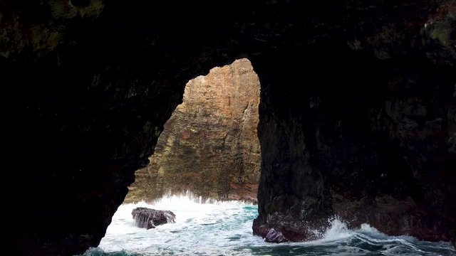 4K Hawaii Kauai Boating on ocean floating looking through rocky arch to rock wall with waves crashing