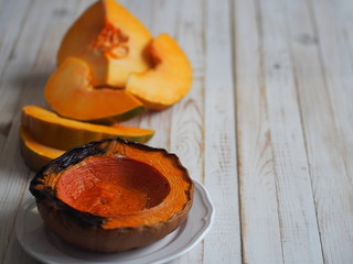 Cooking pumpkins. Home cooking, natural food for vegetarians. Traditional autumn pumpkin dishes. Grilled grilled pumpkin with spices on a background of raw pumpkin on a white wooden table.