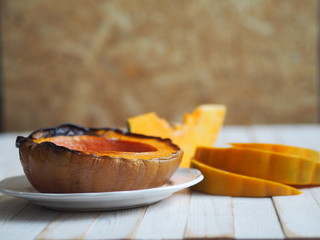 Cooking pumpkins. Home cooking, natural food for vegetarians. Traditional autumn pumpkin dishes. Grilled grilled pumpkin with spices on a background of raw pumpkin on a white wooden table.