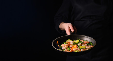 Seafood, shrimp chef cook with vegetables and fire on a black background.Banner, Delicious and healthy vegan cuisine
