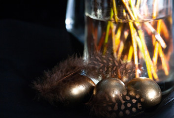 Easter holiday, composition on a dark background. Golden eggs and feathers of partridge in black...