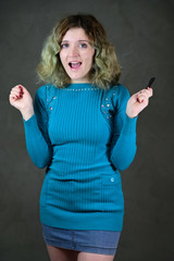 Concept vertical photo of a young woman with emotions in a blue dress. Portrait of a pretty student girl with beautiful curly hair is standing in front of the camera on a gray background.