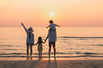 Happy family having fun standing hand in hand on beach at sunset Father gives son to ride on shoulder.