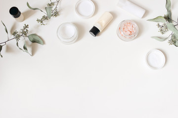 Styled beauty frame, web banner. Skin cream, shampoo bottle, dry eucalyptus leaves and pink Himalayan salt. White table background. Organic cosmetics, spa concept. Empty space, flat lay, top view.