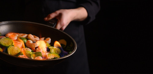 Seafood, shrimp chef cook with vegetables and fire on a black background.Banner, Delicious and healthy vegan cuisine