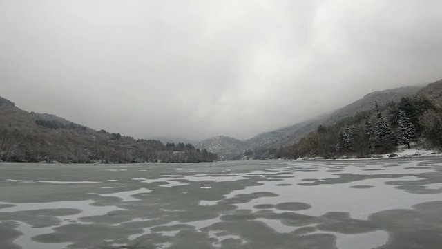 Aerial drone bird's eye view of frozen lake covered with snow at winter time and bubbless of deep gas on the surface