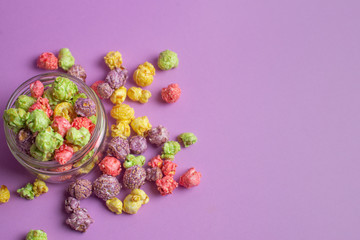 Multicolored fruit flavored popcorn in glass cups on pink background. Candy coated popcorn.