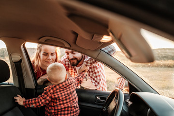 Happy Young Family Mom and Dad with Their Son Little Driver Enjoying Summer Weekend Picnic on the Car Outside the City in the Field at Sunny Day Sunset, Vacation and Road Trip Concept