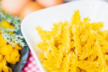 Pâtes torsades crues dans bol blanc et oeufs sur la table de cuisine	