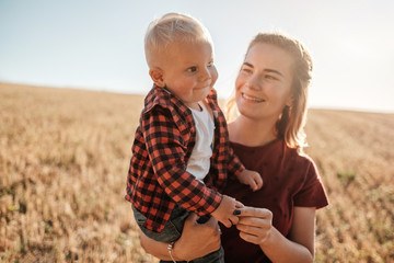 Fototapeta na wymiar Happy Mom with Her Little Son Enjoying Summer Weekend Outside the City in the Field at Sunny Day Sunset