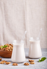 Organic non dairy walnut milk in glass and wooden plate with walnuts on a gray concrete background.