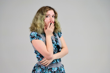 Fototapeta premium Concept horizontal photo of a young woman with emotions in a turquoise dress stands in front of the camera on a white background. Portrait of a student girl with beautiful magnificent hair.