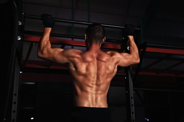 Fototapeta na wymiar Strong masculine man athlete doing pull ups o dark fitness club background. Closeup portrait.