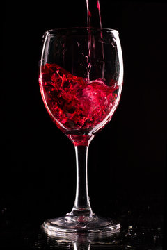 a wine glass on a dark background is filled with a red drink.