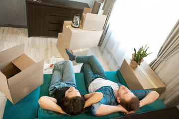 young couple man and woman looking tired having break on the sofa during moving to new appartment unpacking boxes