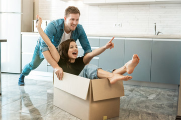 young couple husband and wife looking happy having fun while unpacking and moving in new appartment. husband carrying his wife in box on the floor