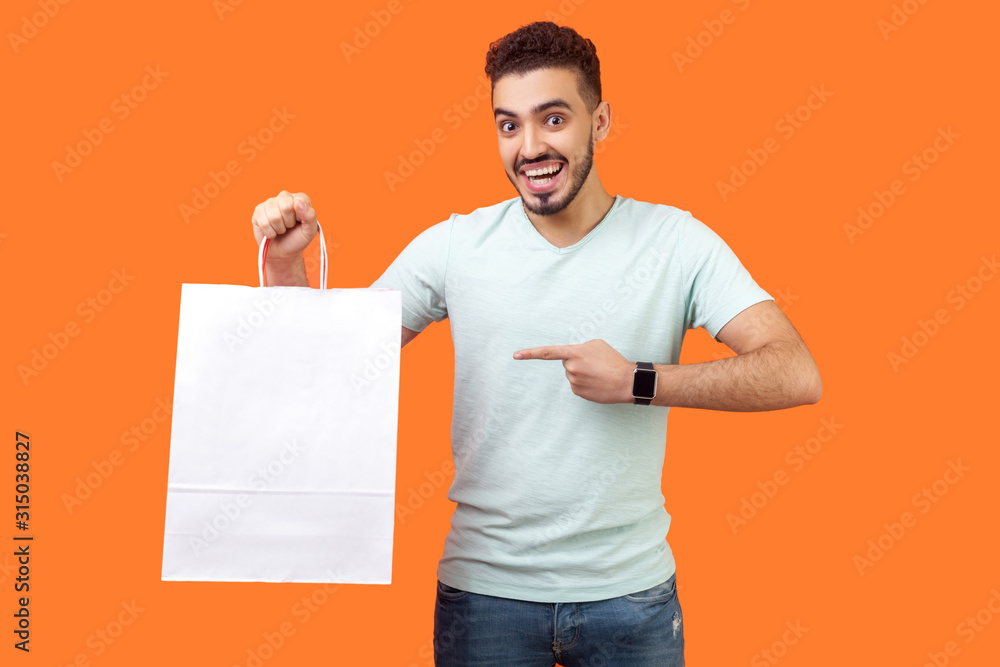 Wall mural portrait of joyous buyer, brunette man with beard in white t-shirt smiling and pointing at packages,