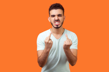 Portrait of furious aggressive brunette man with beard in white t-shirt showing middle fingers, impolite rude gesture of disrespect, fuck off expression. studio shot isolated on orange background