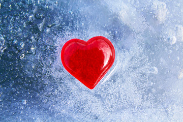 Red glass heart on blue ice. Close-up. Top view. Background. Texture.