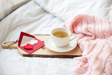 Beautiful white cup with tea on the bed, pink knitted plaid, postcard Happy Valentine's Day. Breakfast in bed. Morning. Spring. Cozy.