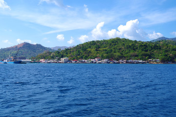 Fototapeta na wymiar A small, colorful town hugging the coast of an island in the Philippines archipelago. It's a beautiful, sunny, summer day and the waters of the ocean are very blue and calm. 